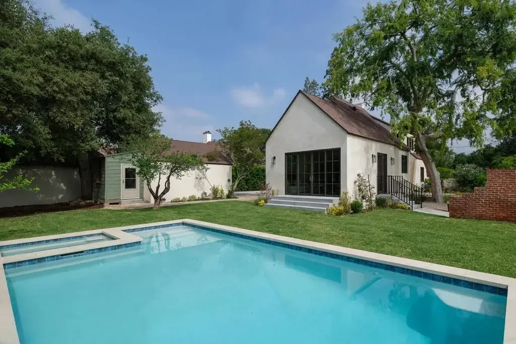Pool surrounded by lawn with a gabled building beyond